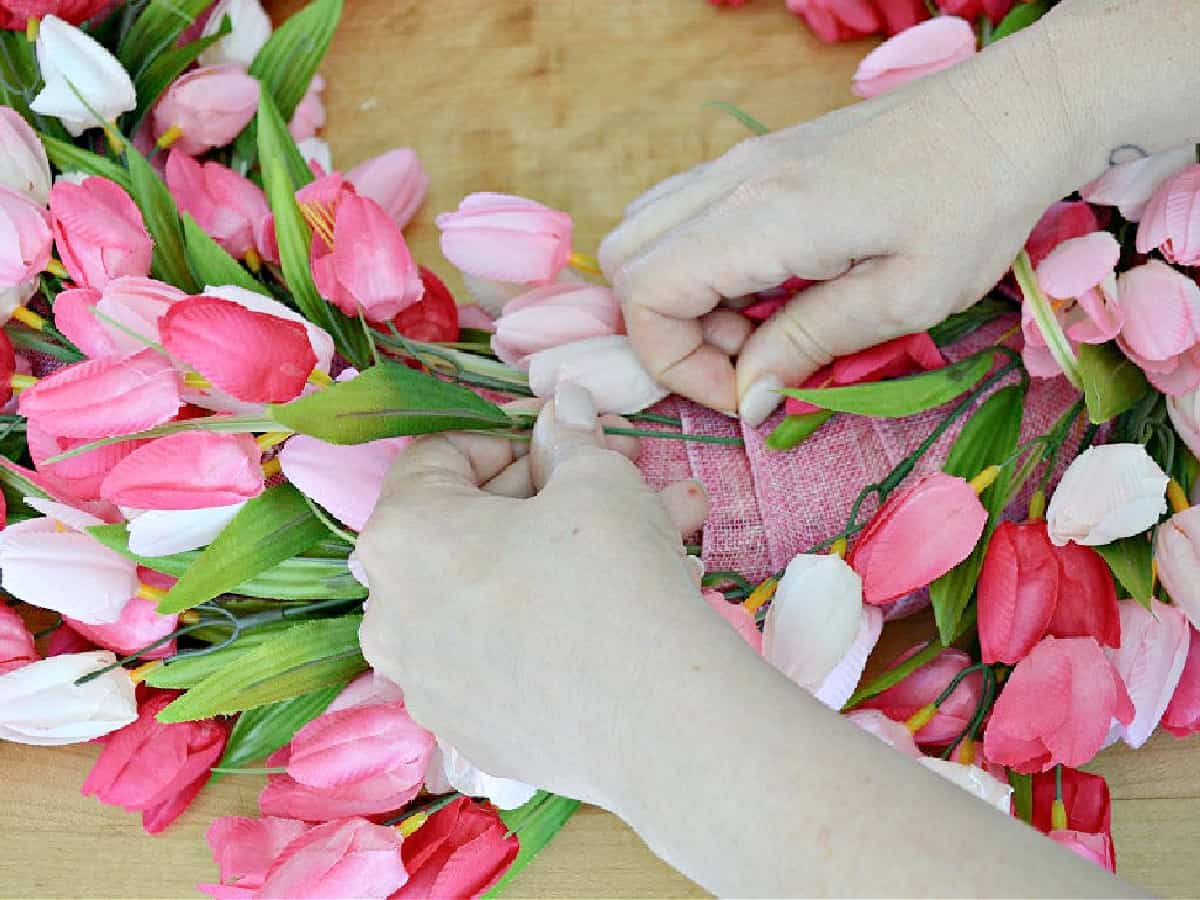 inserting pink tulip stem in ribbon wrapped wreath form