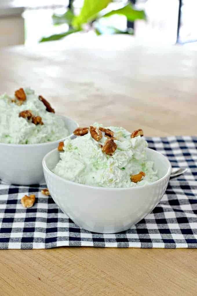 green stuff in white bowl with chopped pecans sprinkled on top