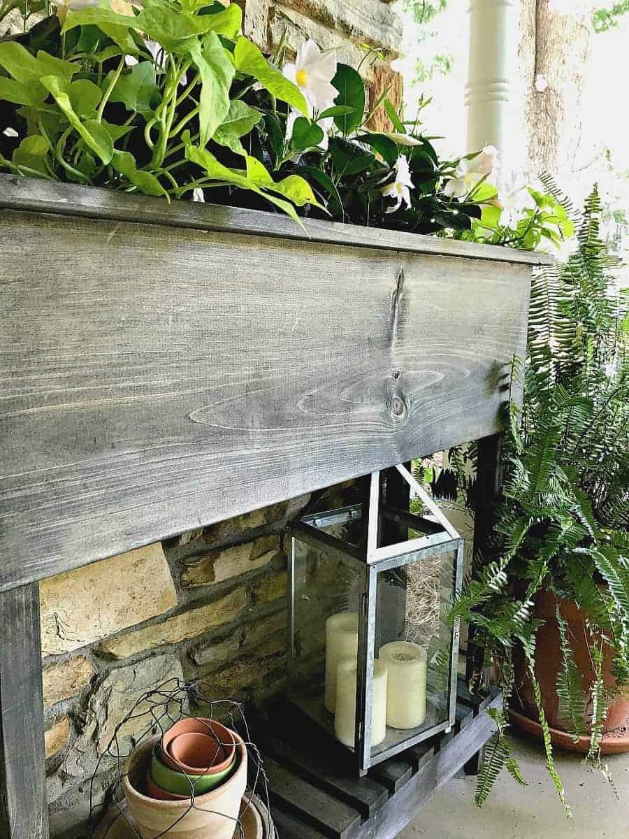 DIY wood raised planter with legs on front porch with white flowers planted in it.