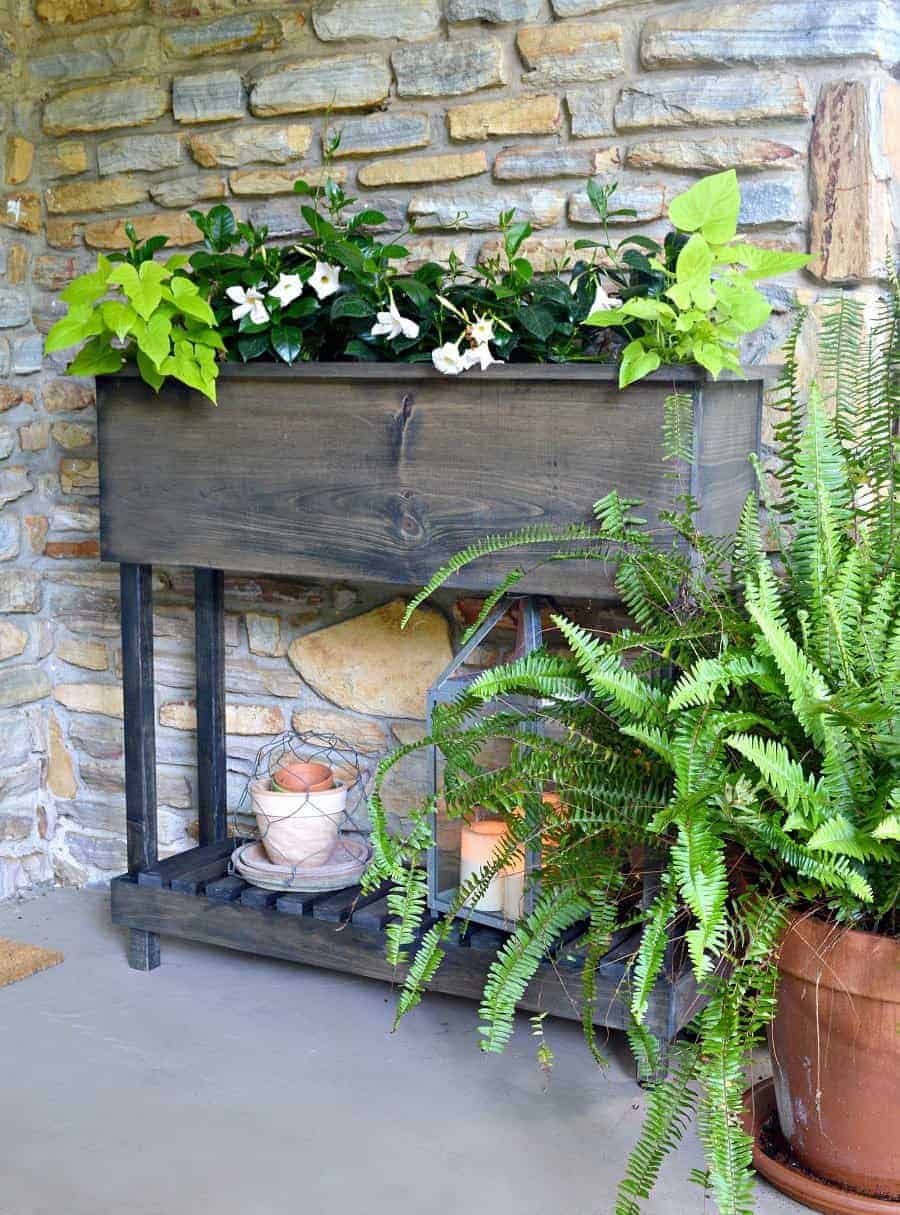 finished DIY wood raised planter box with legs with flowers planted in it and old pots on bottom shelf