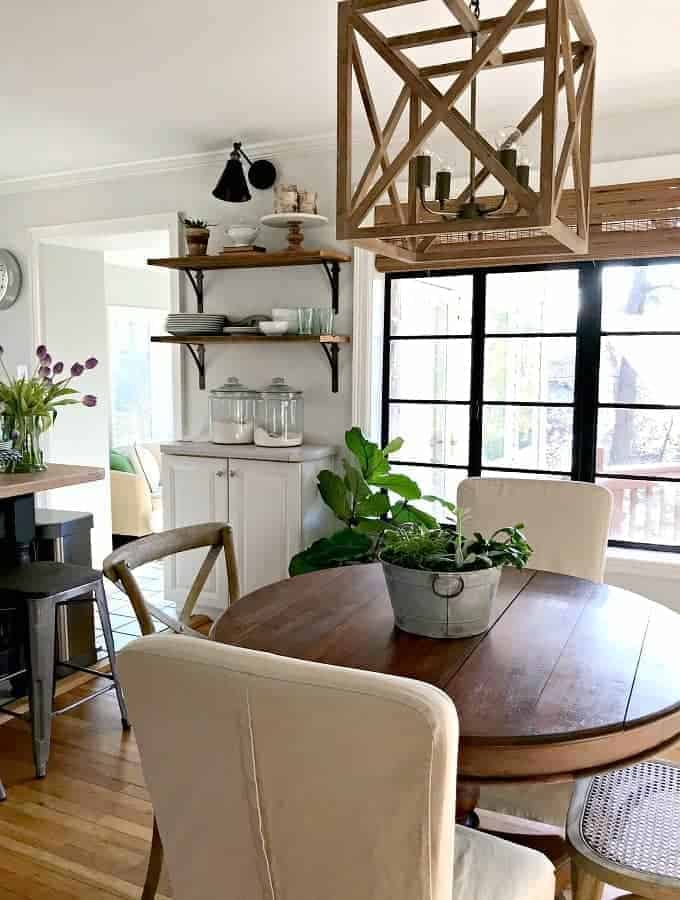 round kitchen table with wood hanging fixture above it and barn wood shelves in the background