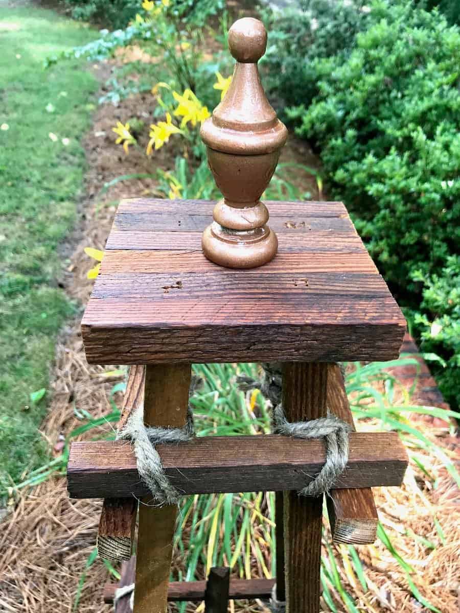 top half of a wooden garden obelisk sitting in the middle of a garden with daylilies