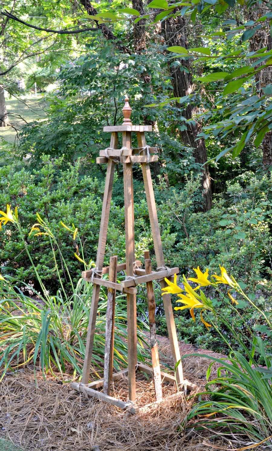 wooden garden obelisk sitting in the middle of a wooded garden with daylilies