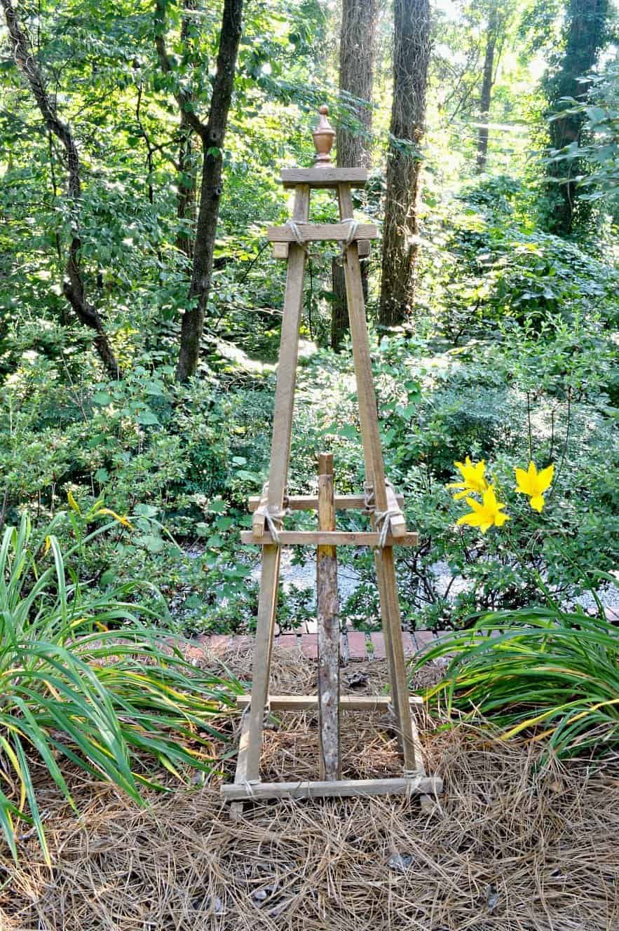 a DIY wooden garden obelisk sitting among the daylilies in a garden