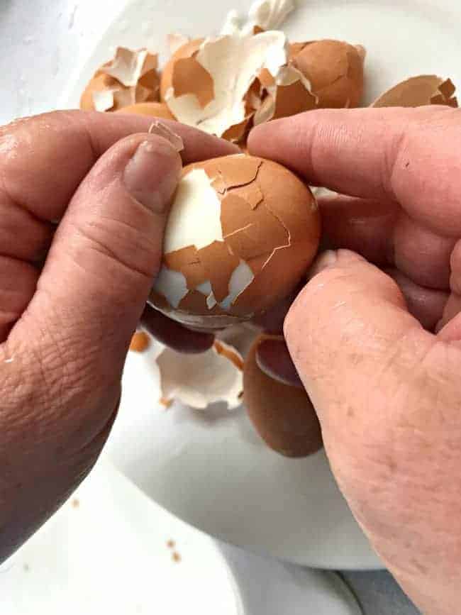 man's hands peeling hard boiled egg