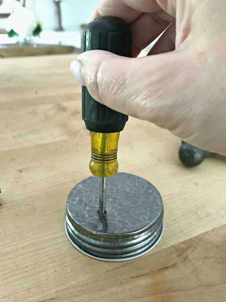 making DIY mason jar lanterns, using an awl to poke holes in mason jar lid