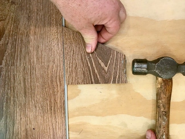 tapping scrap piece of vinyl plank flooring with a hammer 