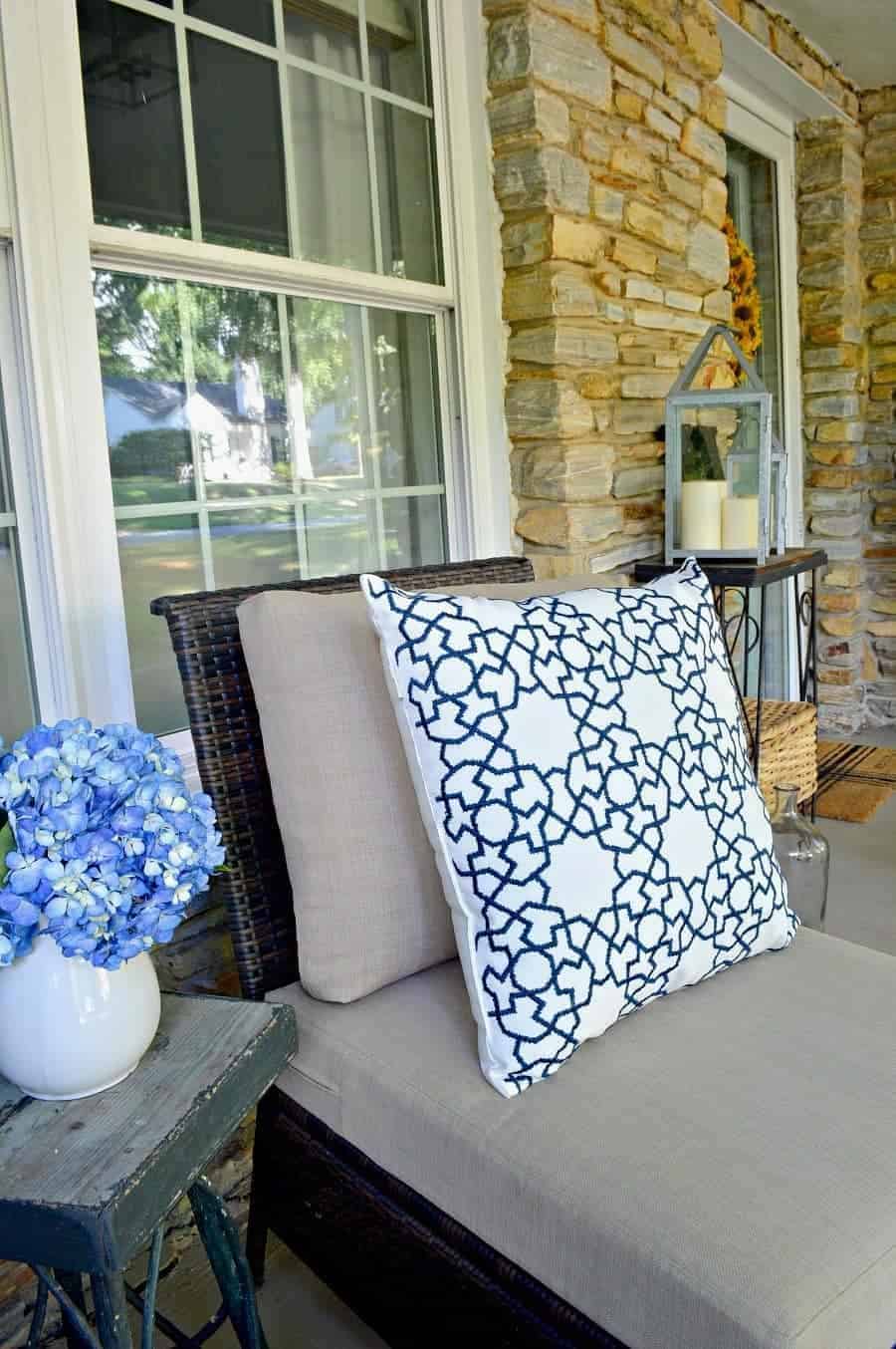 wicker chair on porch with blue and white pillows and blue hydrangeas in a white pitcher