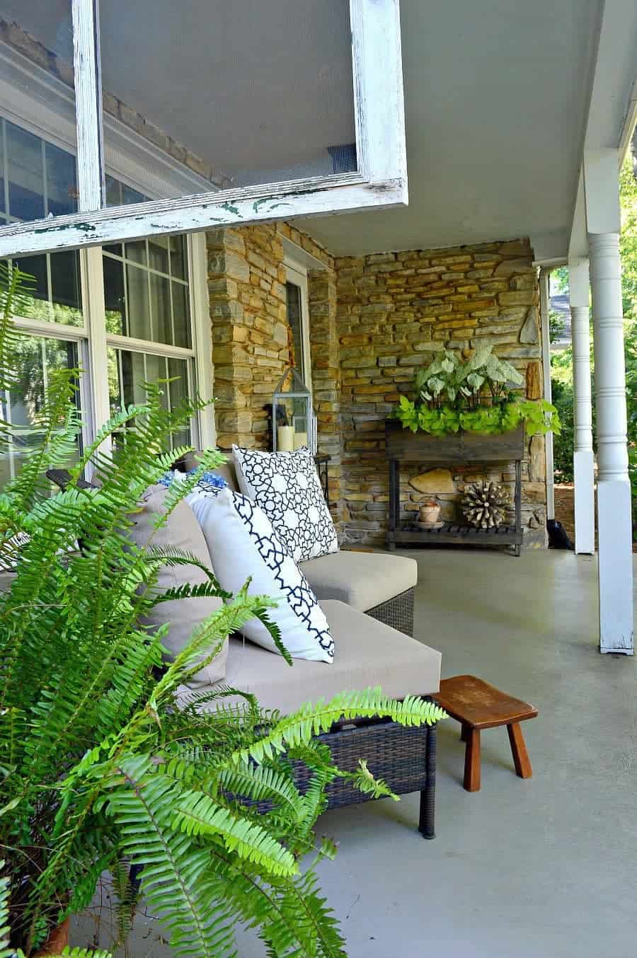 two wicker chairs on porch with blue and white pillows, a little footstool and a green potted fern