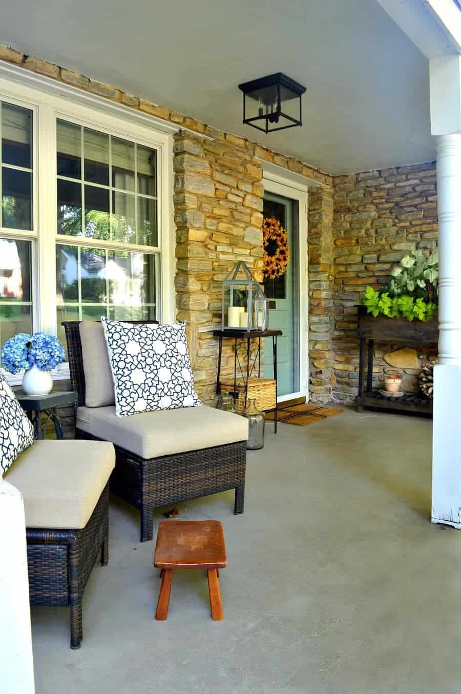 two wicker chairs on porch with blue and white pillows, a little footstool and a blue door with a sunflower wreath