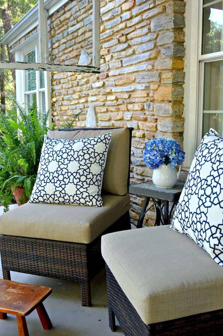 two wicker chairs on covered porch with blue and white pillows, a little footstool and a hanging screen window