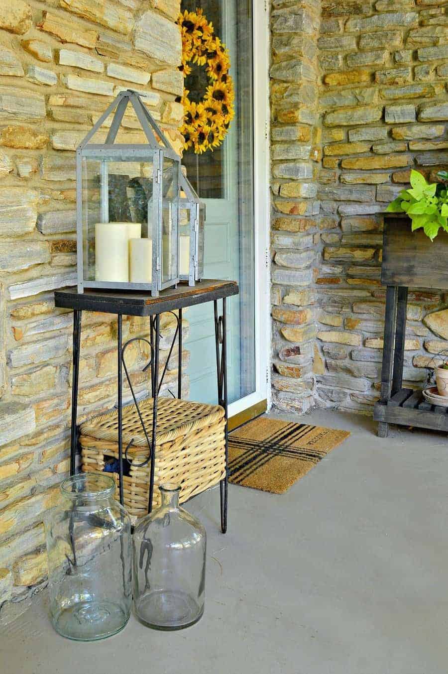 wood table with metal lanterns, a wicker box and two large bottles sitting on the ground. 