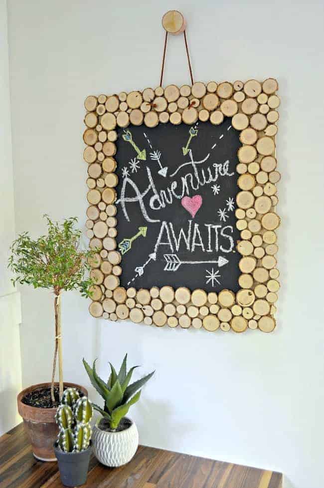 Rustic Wood Slice Chalkboard hanging on white wall with 3 green plants sitting on a wood countertop.