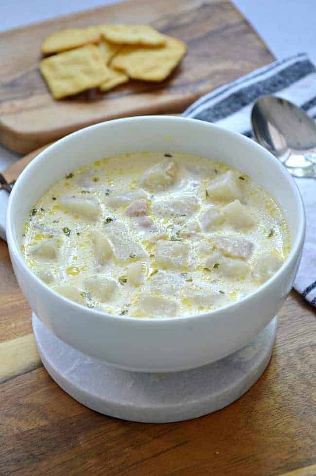 bowl of easy New England Clam Chowder sitting on wood cutting board with 2 spoons and crackers on another cutting board.