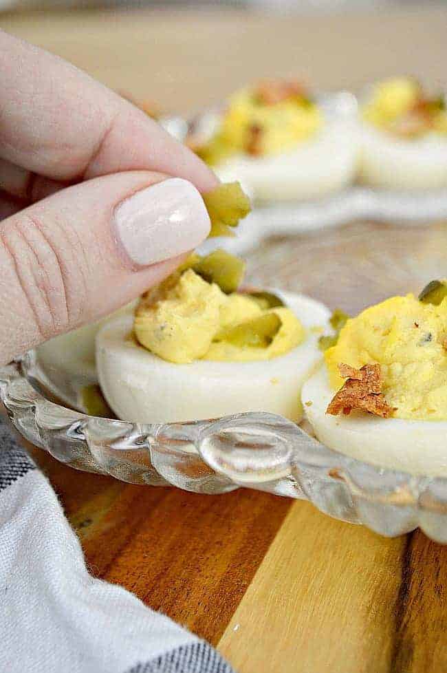 placing sweet pickle pieces on deviled eggs in egg tray