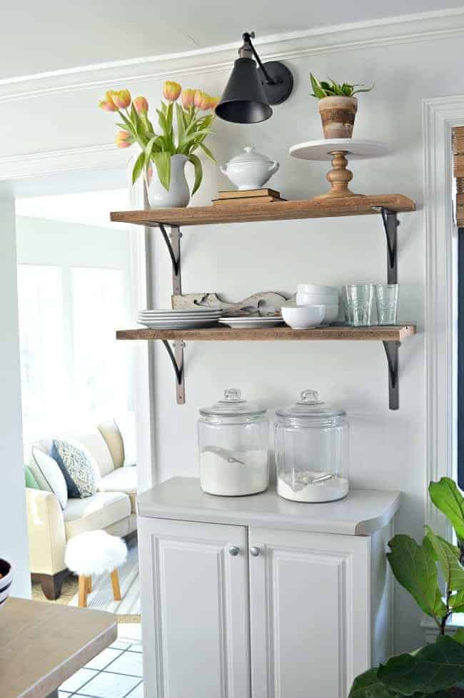 How to Make a DIY Wireless Wall Sconce Image DIY wireless wall sconce hanging over kitchen open shelving with dishes and a pitcher of tulips