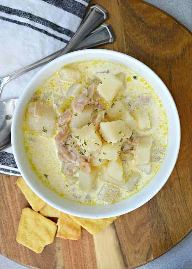a bowl of New England Clam Chowder on a cutting board with crackers and 2 spoons is just one of 12 of the best soups to make 