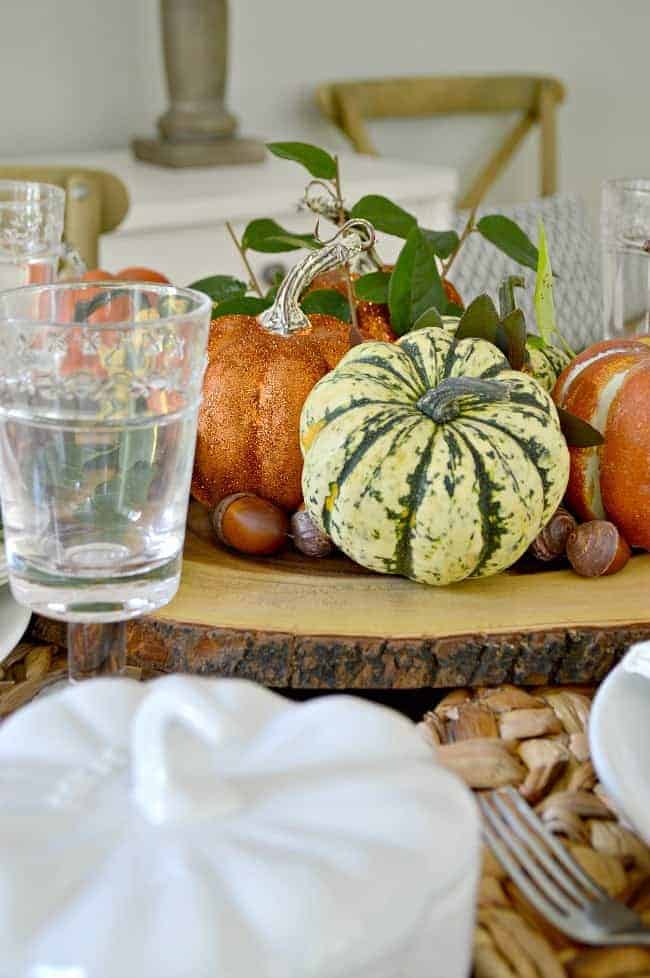 DIY glitter pumpkins, faux pumpkins and pumpkin squash on wood round in center of table.