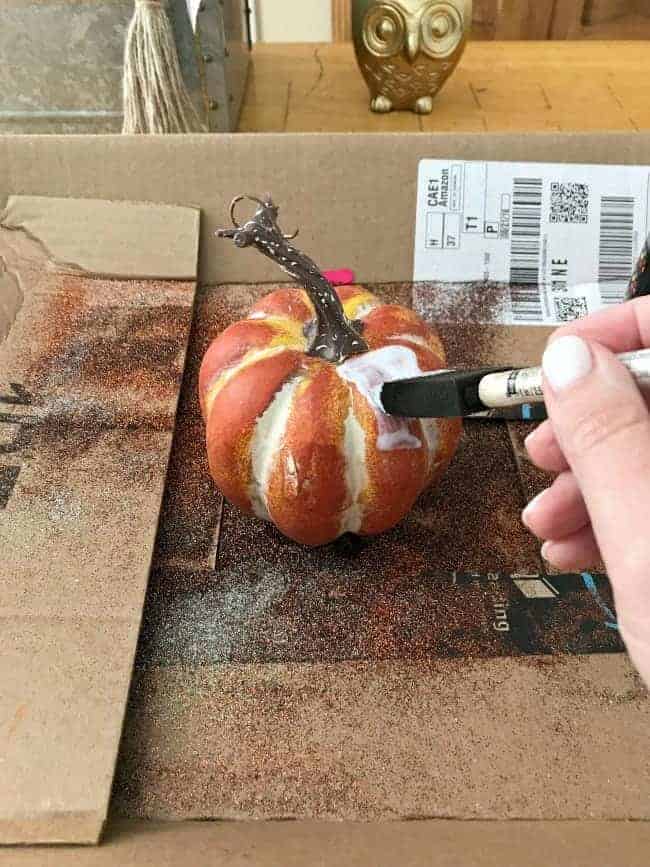 applying Mod Podge on faux pumpkin to create DIY glitter pumpkins