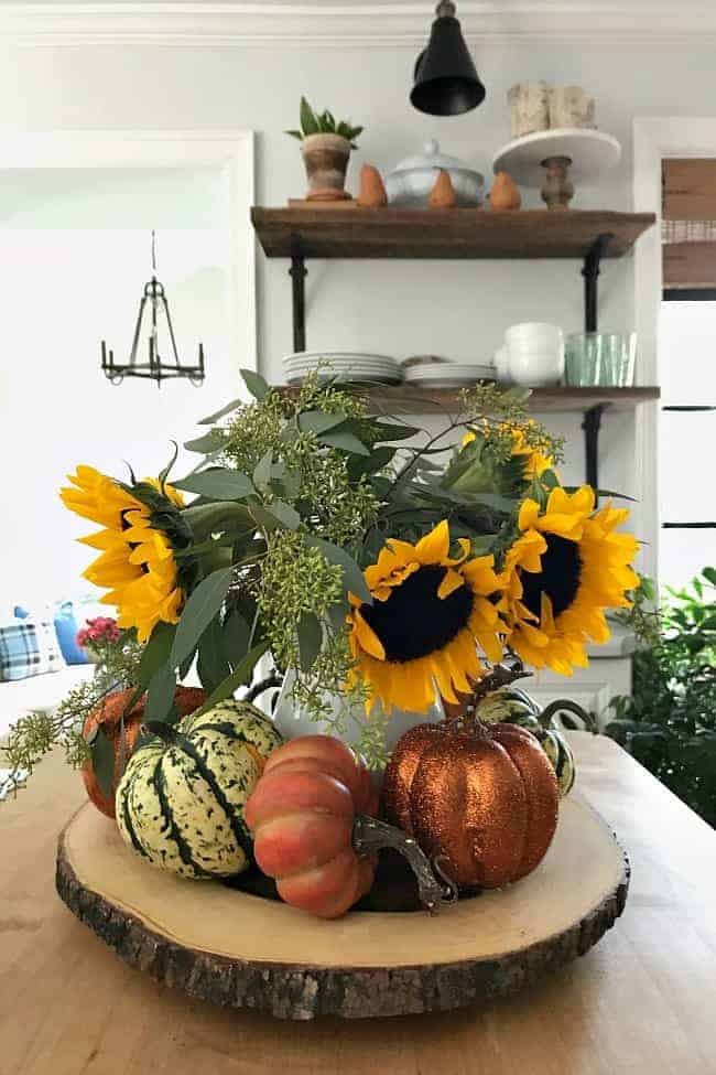 centerpiece with pitcher of sunflowers and DIY glitter pumpkins on wood round