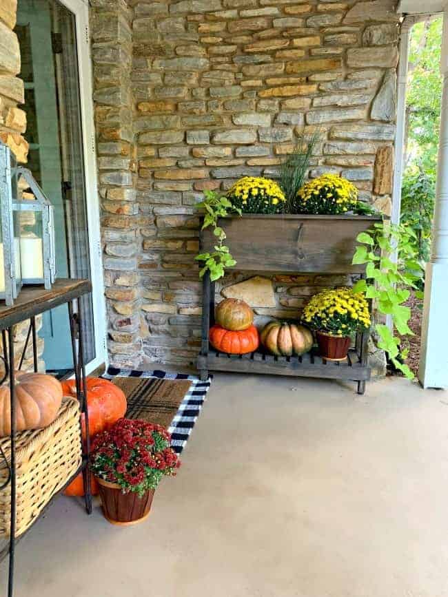 front porch fall decor with a planter filled with mums and pumpkins on a bottom shelf