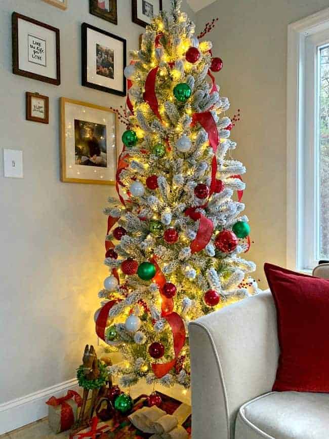 a flocked Christmas tree in the corner of a sunroom with red and green decor and presents underneath