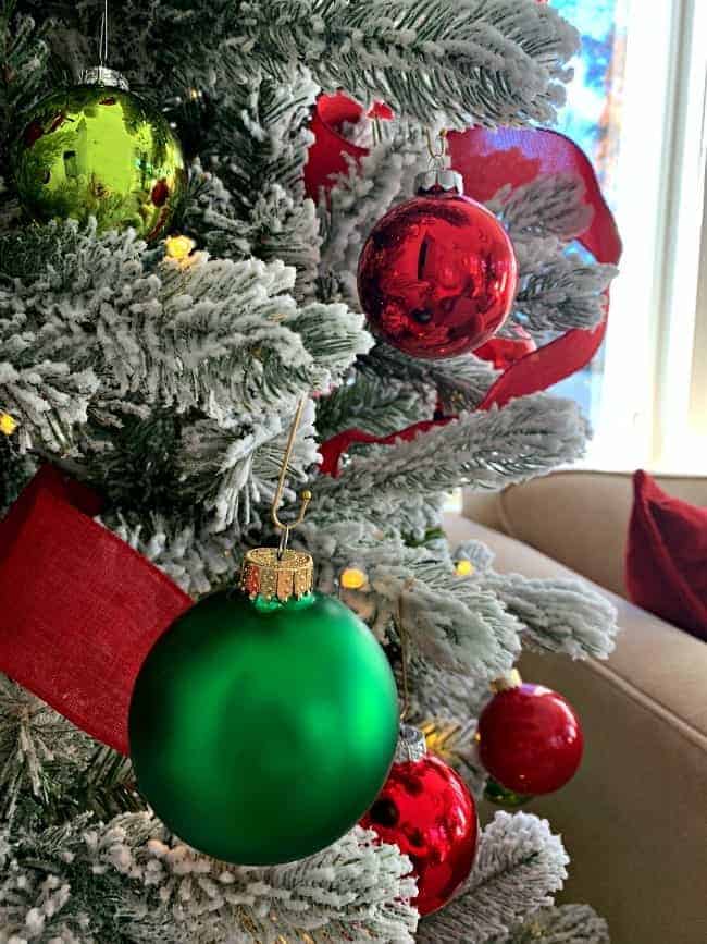 a close-up view of red and green glass ornaments on a flocked Christmas tree