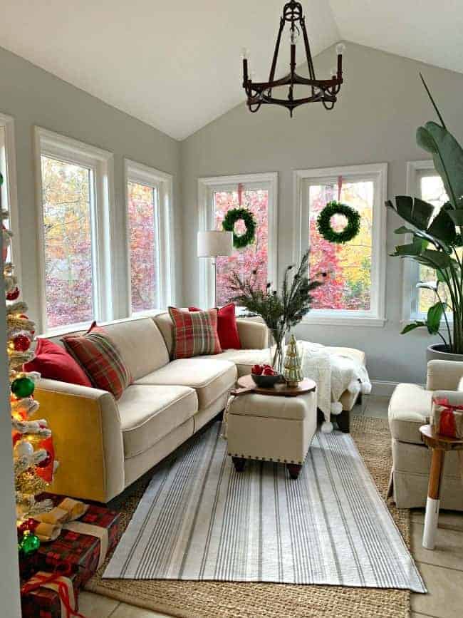 corner view of a sunroom with a peak of the tree, a sectional sofa and a large bird of paradise plant in the corner