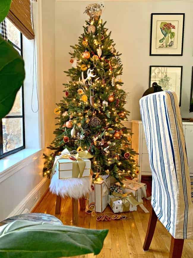 A Rustic Christmas Tree in a corner with wrapped presents and a fur stool underneath it.