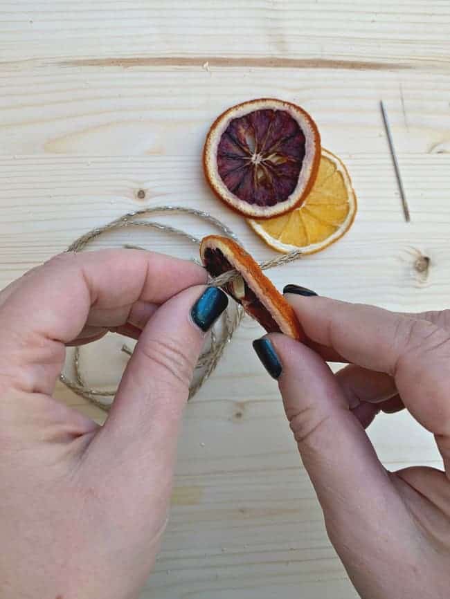 threading thin jute twine through hole in dried blood orange slice