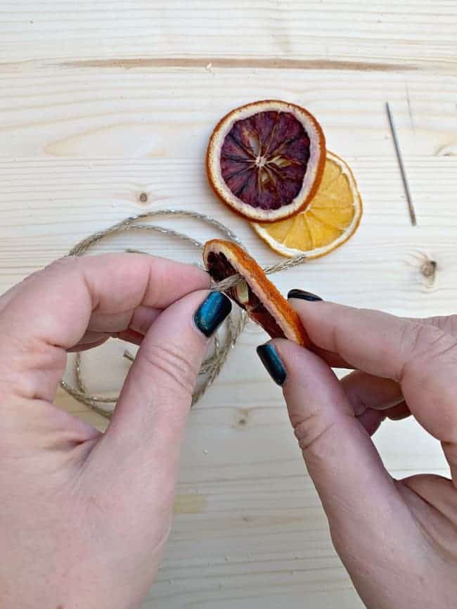 threading jute twine through dried orange slices