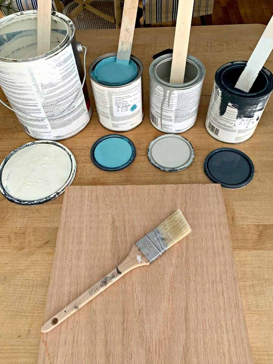 4 open cans of paint and a piece of oak wood with a paintbrush on top