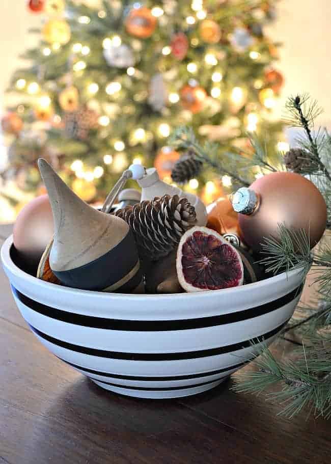 wooden and glass ornaments in a black and white striped bowl on a dining room table