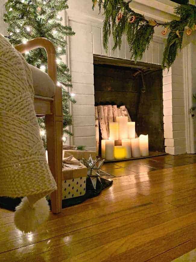 a white brick fireplace with lighted candles inside and greens hanging from the mantle