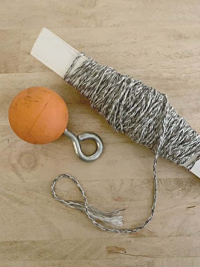 orange lacrosse ball with an eye bolt and a stick with string wrapped around it. 