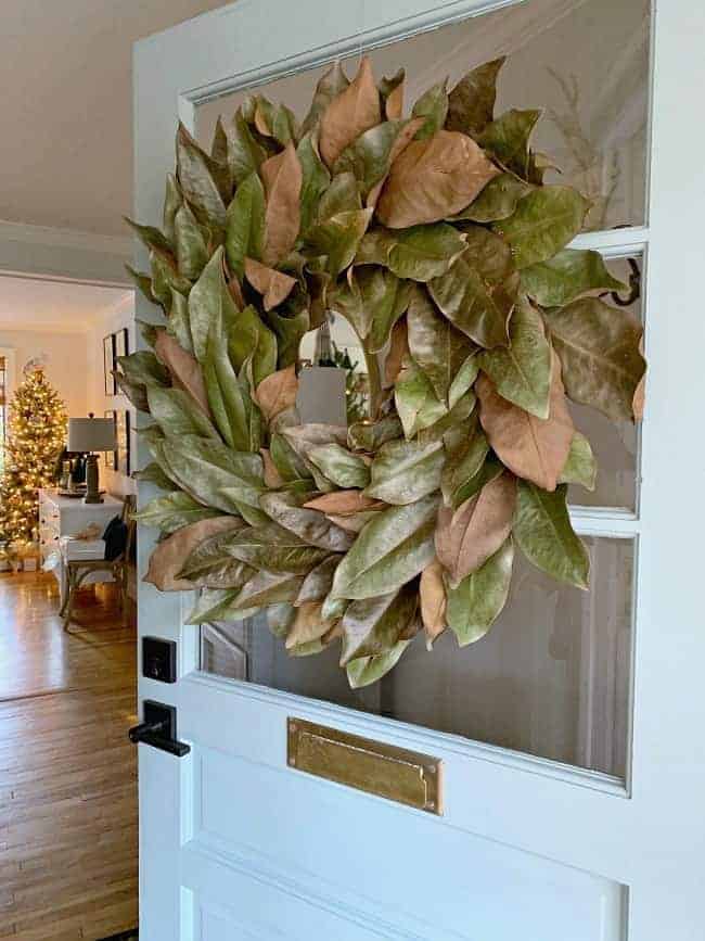 A Cozy Christmas Cottage with a magnolia leaf wreath hanging on the blue front door