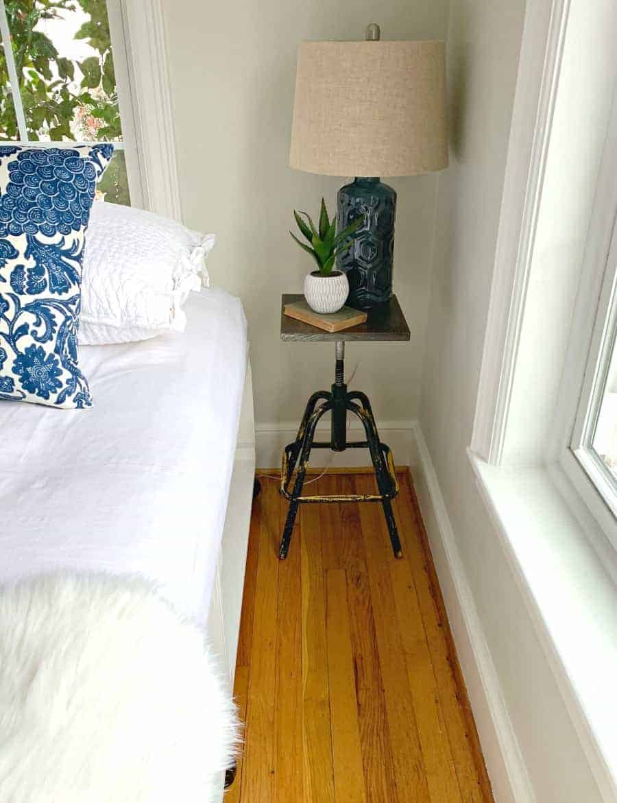 DIY nightstand next to bed with blue lamp, book and plant on top 