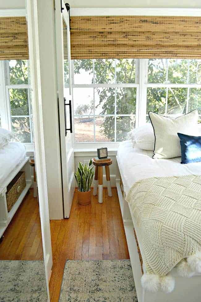 side view of bed with a stool and woven shades in window for guest bedroom makeover