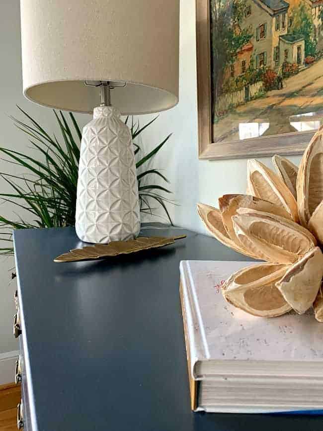 top of navy dresser with lamp, books and seed pod on top