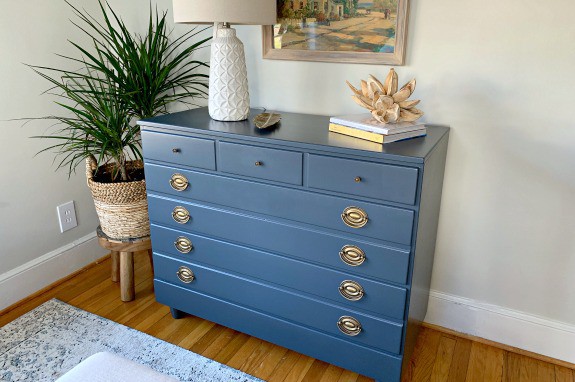 navy painted dresser in guest bedroom with lamp and other decor on top