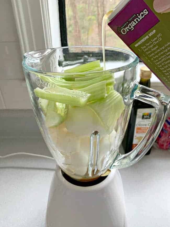 pouring broth into blender with celery and onion in it