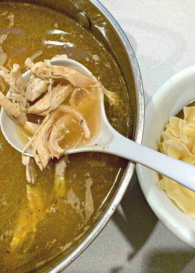 ladling chicken noodle soup into a bowl of noodles