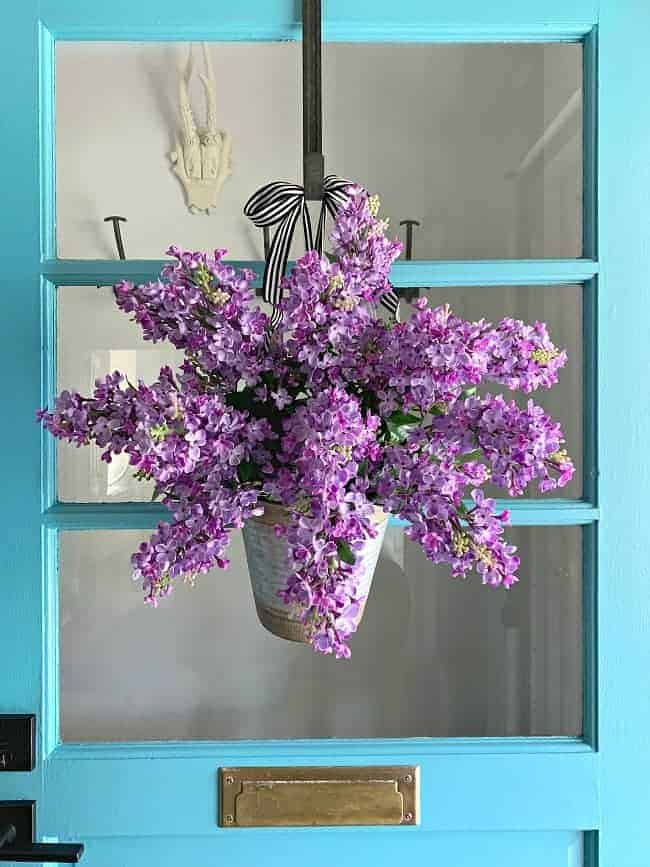 bucket filled with faux lilacs hanging on turquoise front door