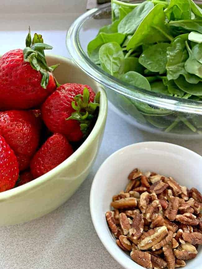 a bowl of strawberries, a bowl of spinach and a small bowl of chopped pecans