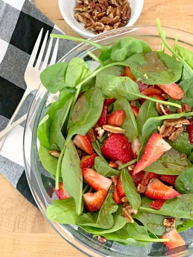 top view of a spinach strawberry salad with poppy seed dressing and a small bowl of chopped pecans