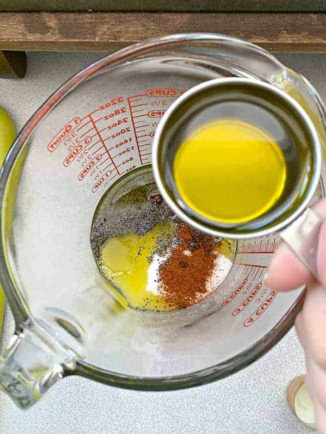 top view of olive oil going into a glass measuring cup with spices in it