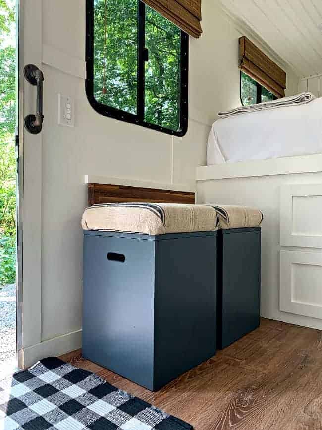 2 navy blue painted storage boxes, with grain sack covered cushions, sitting in front of walnut drop table.