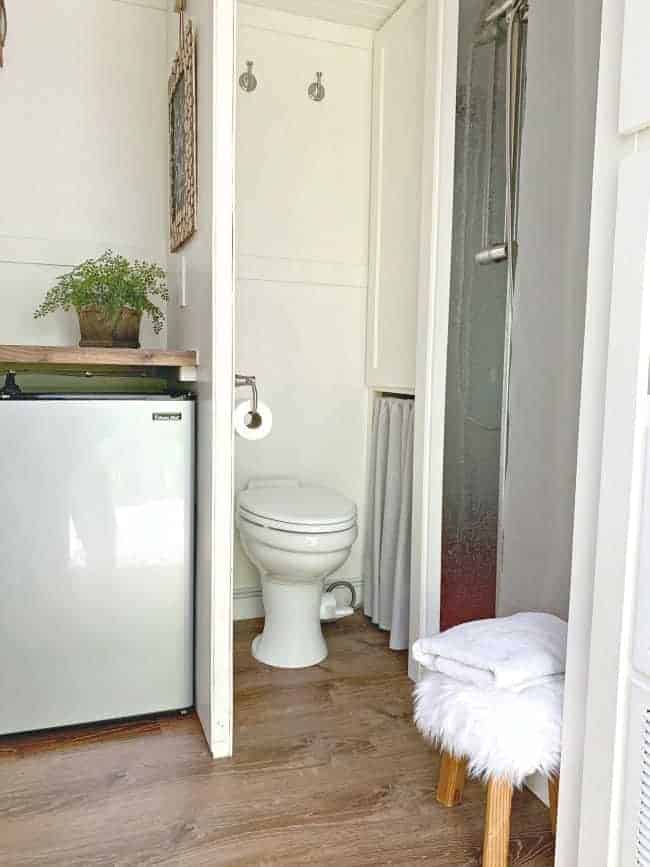 view of a tiny RV bathroom with porcelain toilet and bathroom wall with mini fridge on the opposite side