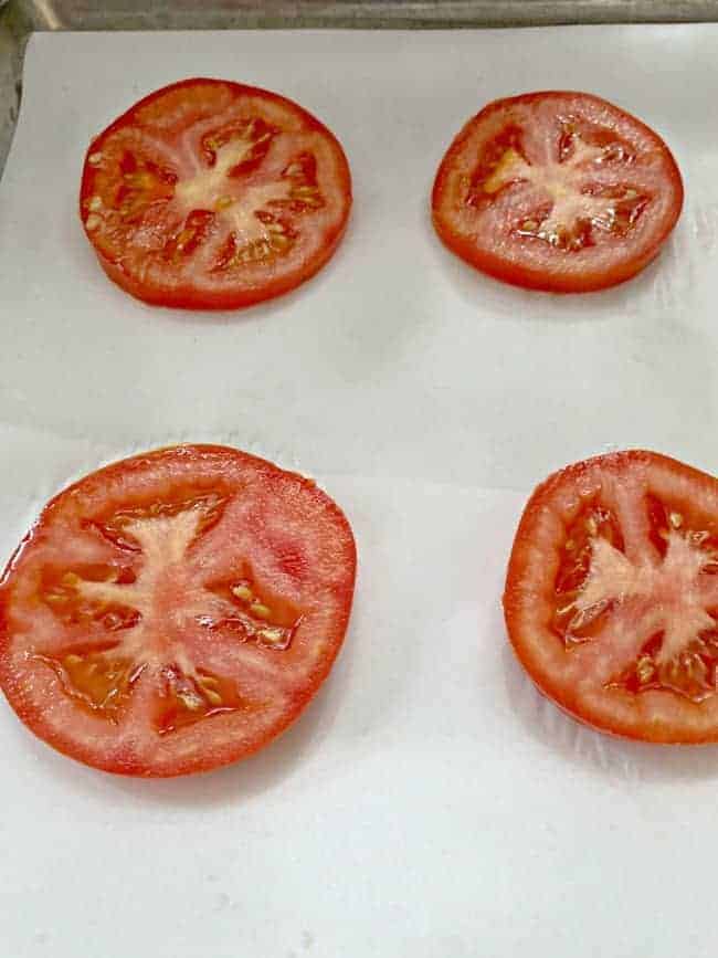 fresh tomato slices on parchment lined cookie sheet