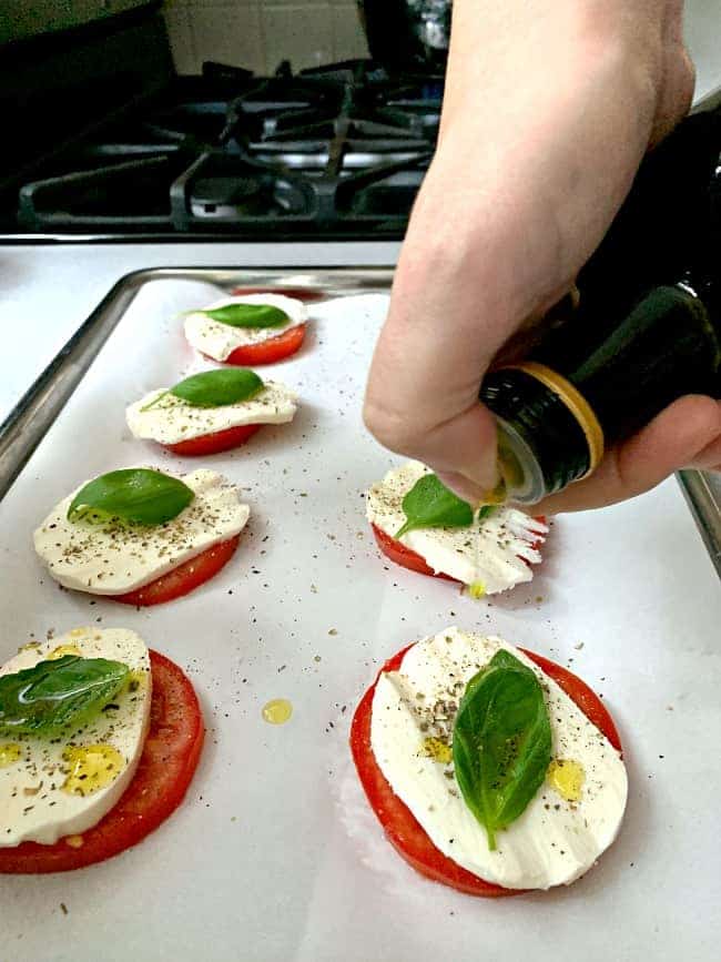 drizzling olive oil on tomato and mozzarella cheese slice with a fresh basil leaf on iy